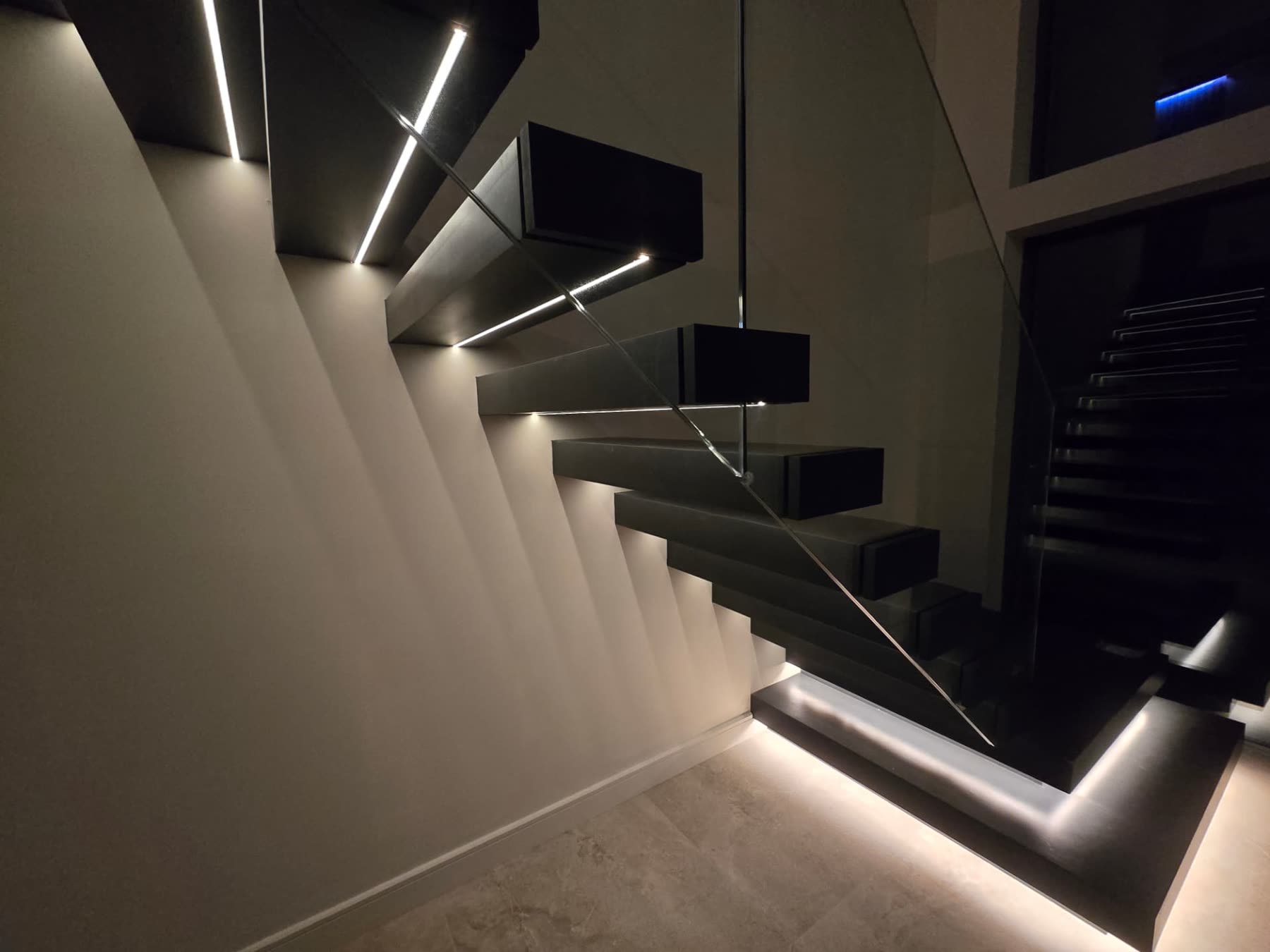 Black floating staircase treads with under-step LED lighting and glass balustrade