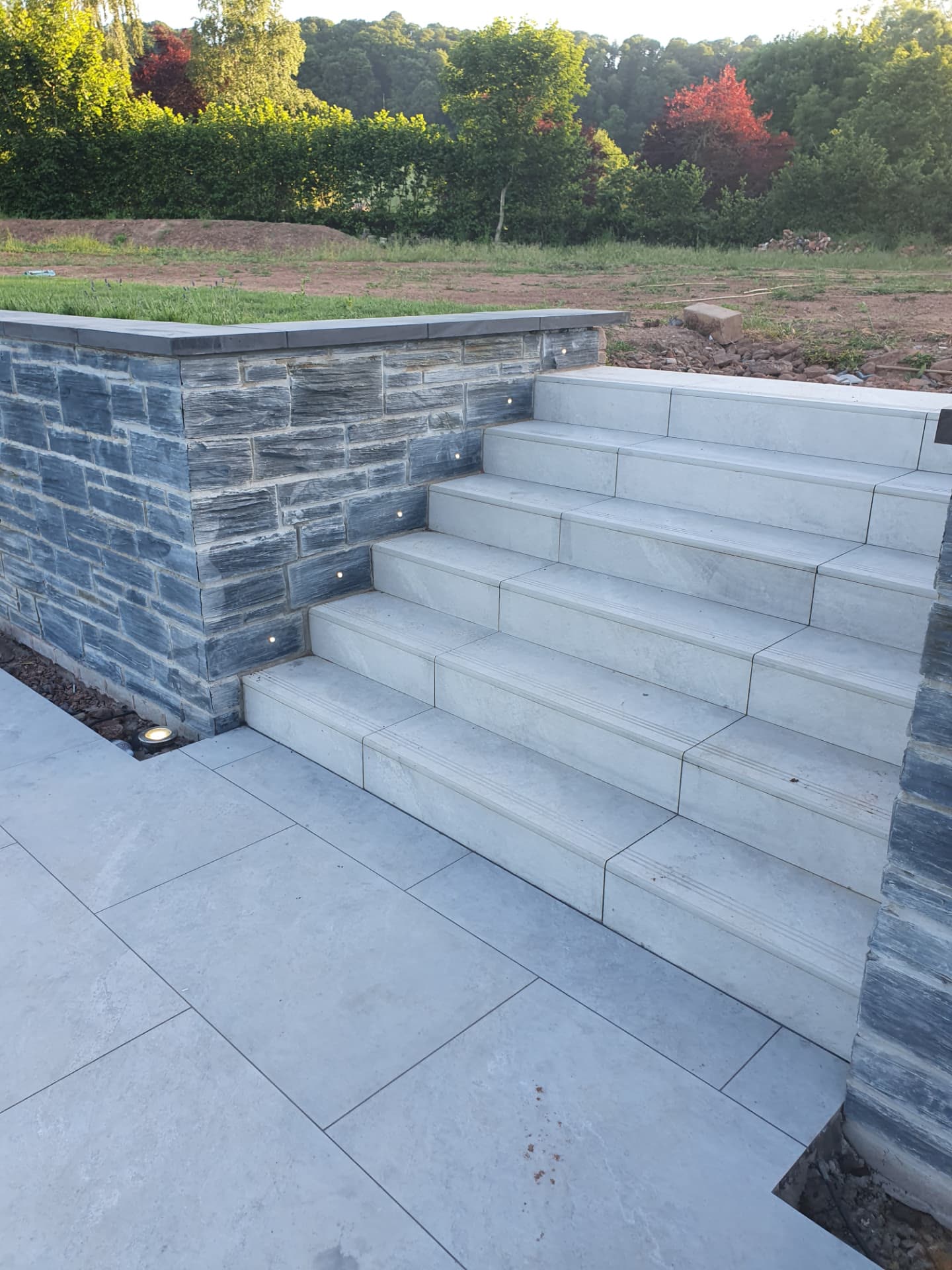 Wide stone steps with built-in lighting rising from a paved terrace at sunset