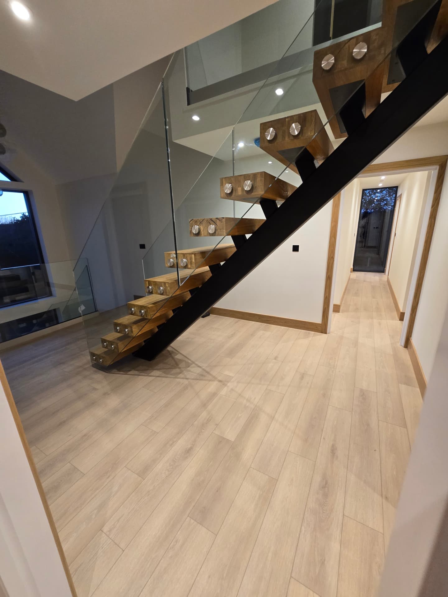 Chunky oak floating staircase built on a black steel spine leading into a hallway