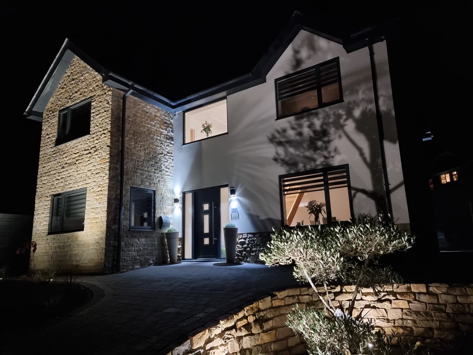 Detached stone and render family home illuminated at night with landscaped front garden