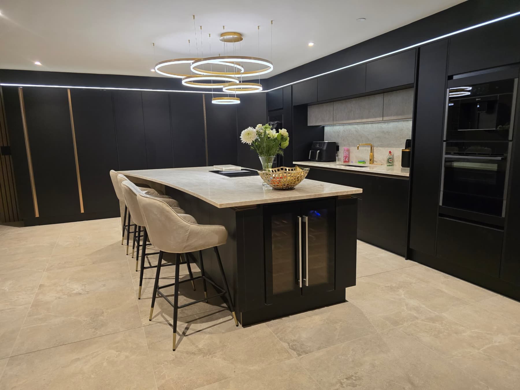 Wide view of a dark bespoke kitchen island with bar stools and brass pendant lighting