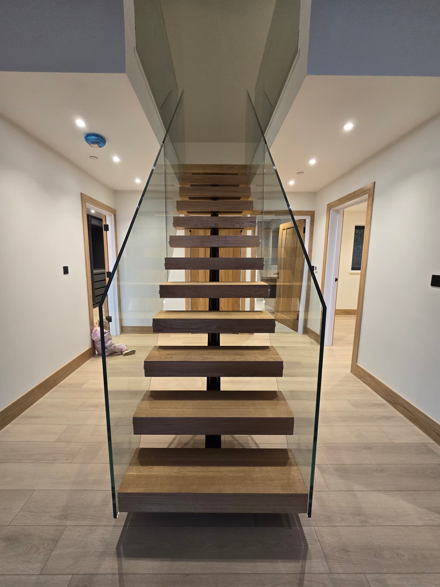 Cantilevered oak staircase with frameless glass balustrade in a modern hallway