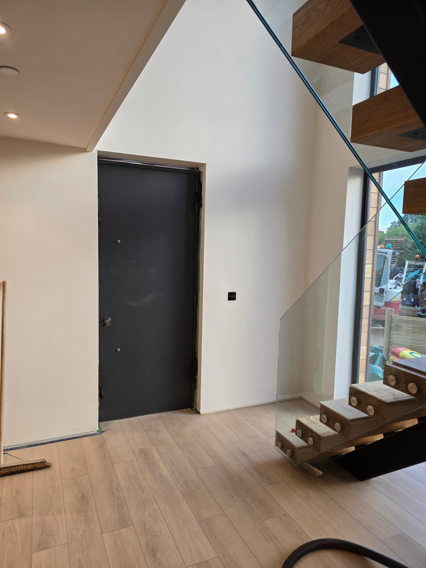 Bright hallway with glass balustrade staircase, timber treads and a dark front door