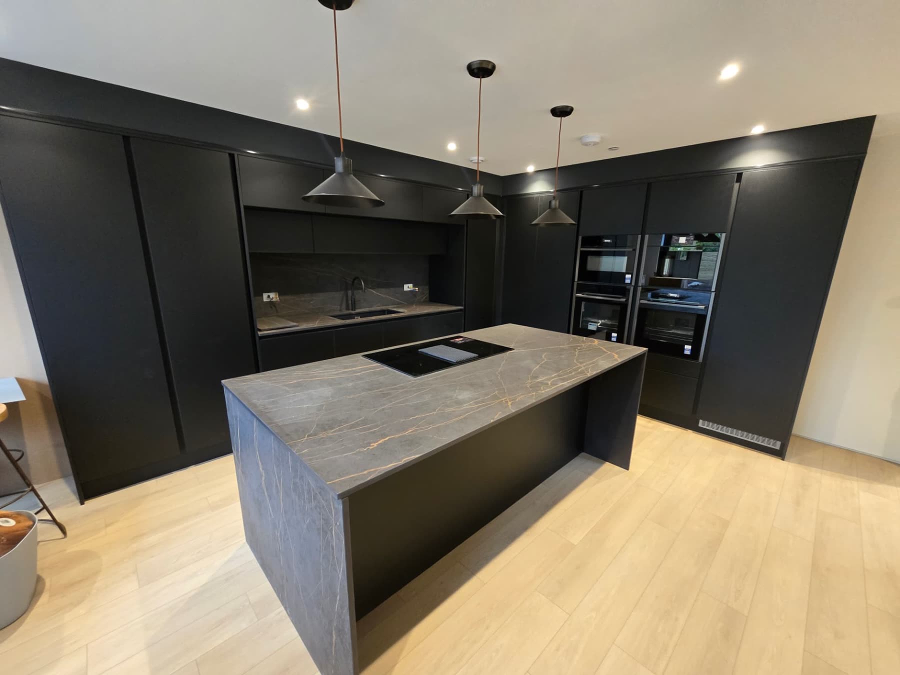 Matte black bespoke kitchen with a large stone-effect island and integrated appliances