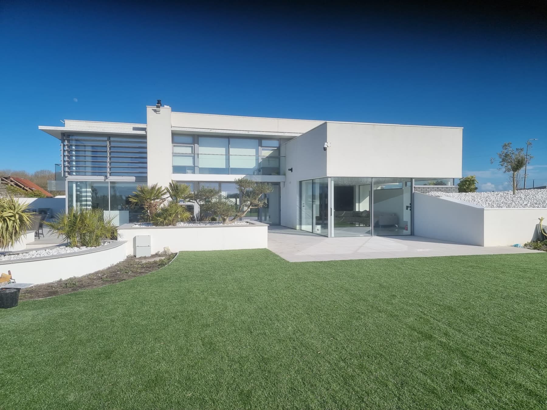 Large modern white rendered house with full-height glazing, terrace and landscaped lawn in South Wales