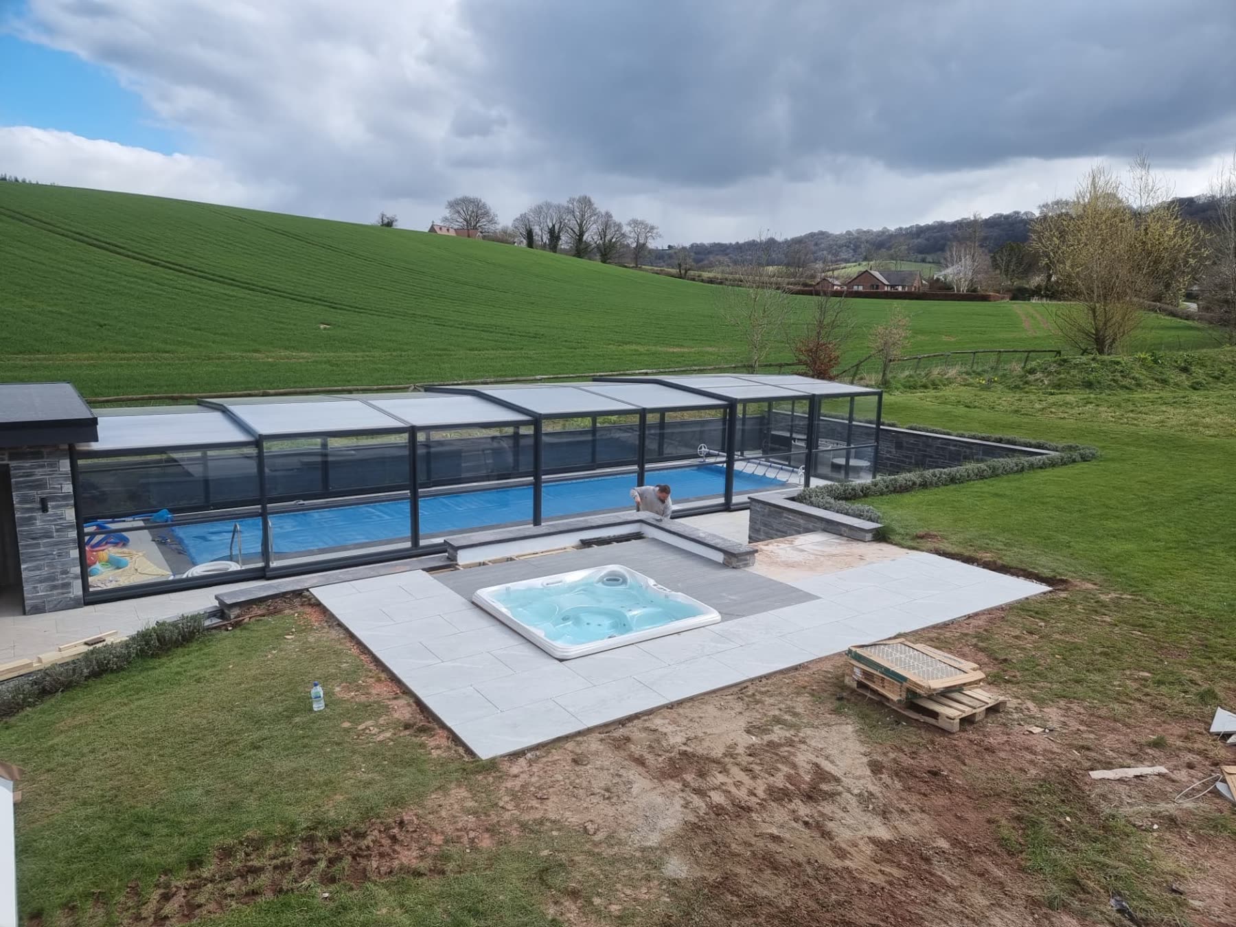 Retractable-roof outdoor pool alongside a new hot tub set into a landscaped country garden