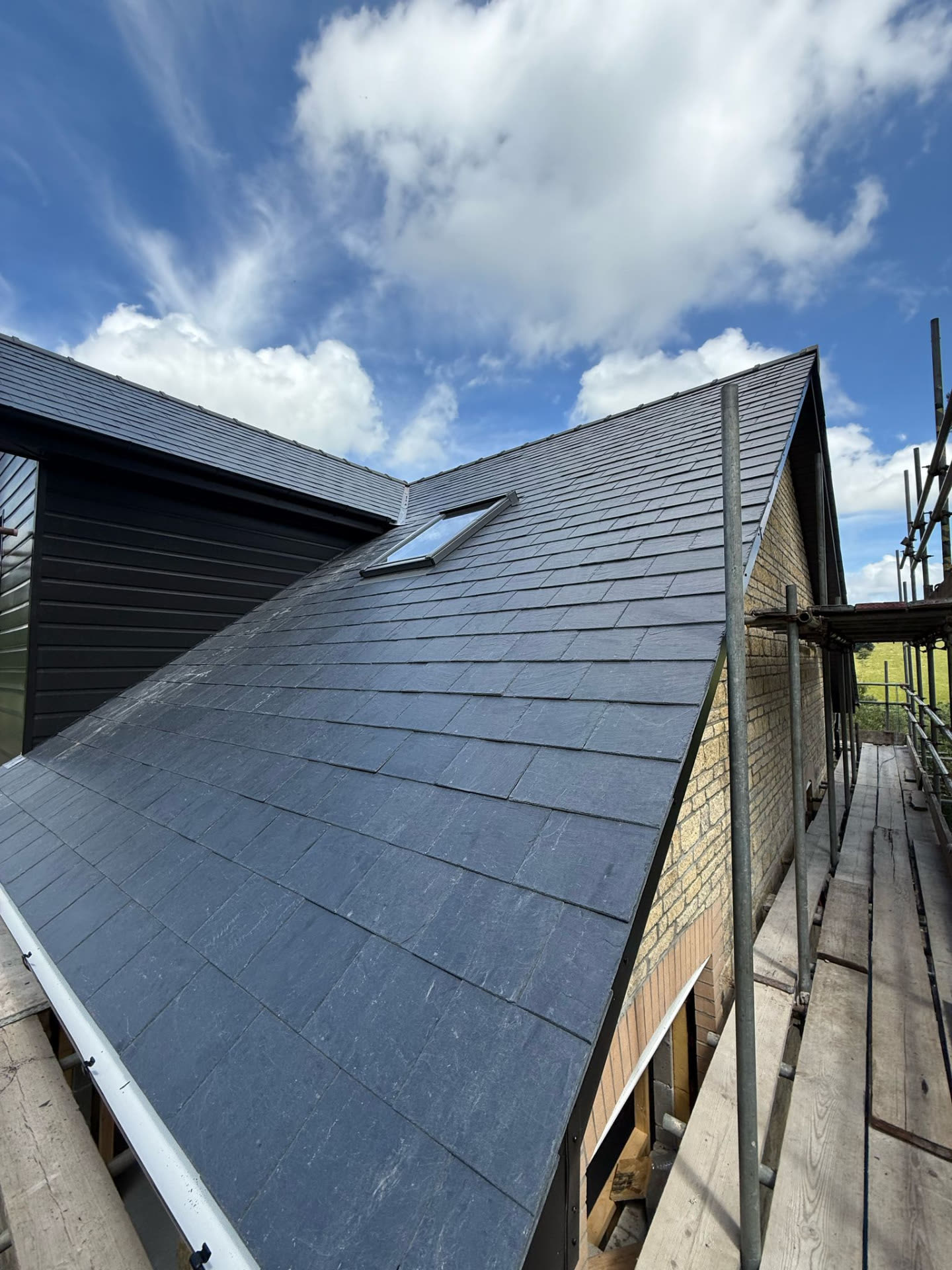 Newly slated roof pitch with roof window, scaffold boards and countryside beyond