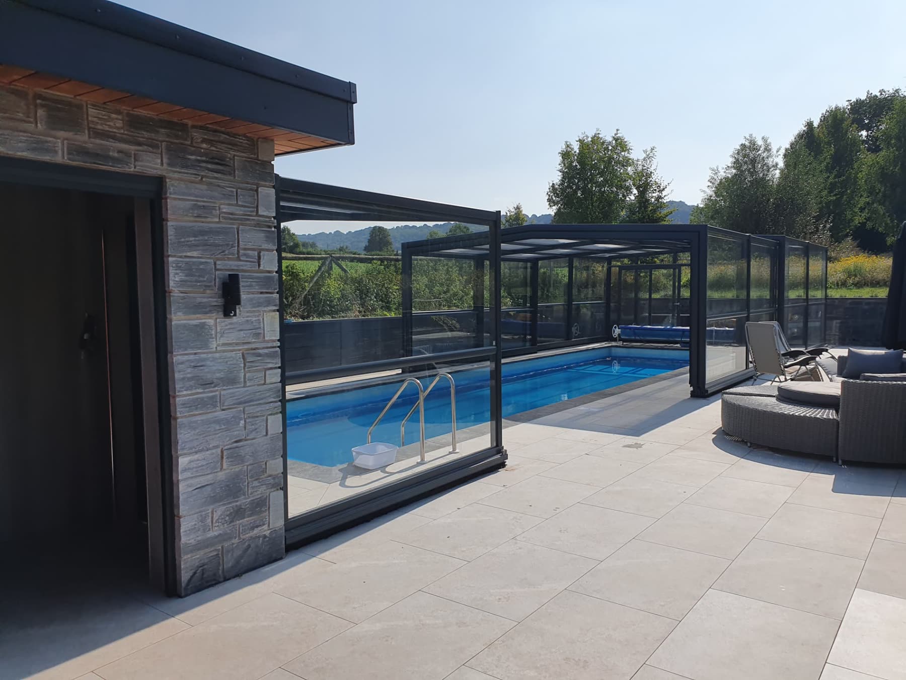 Indoor-outdoor swimming pool beneath a retractable glass canopy with poolside lounge furniture
