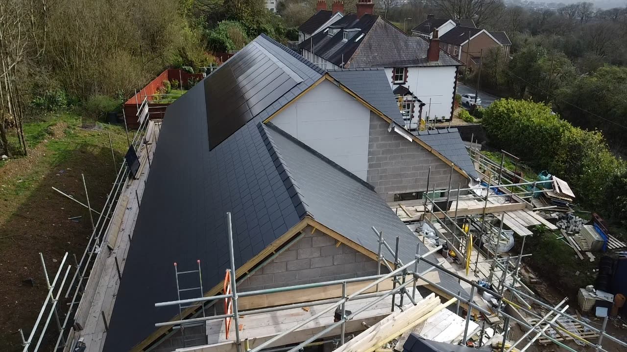 Aerial view of a large slate roof with integrated solar panels on a renovated house