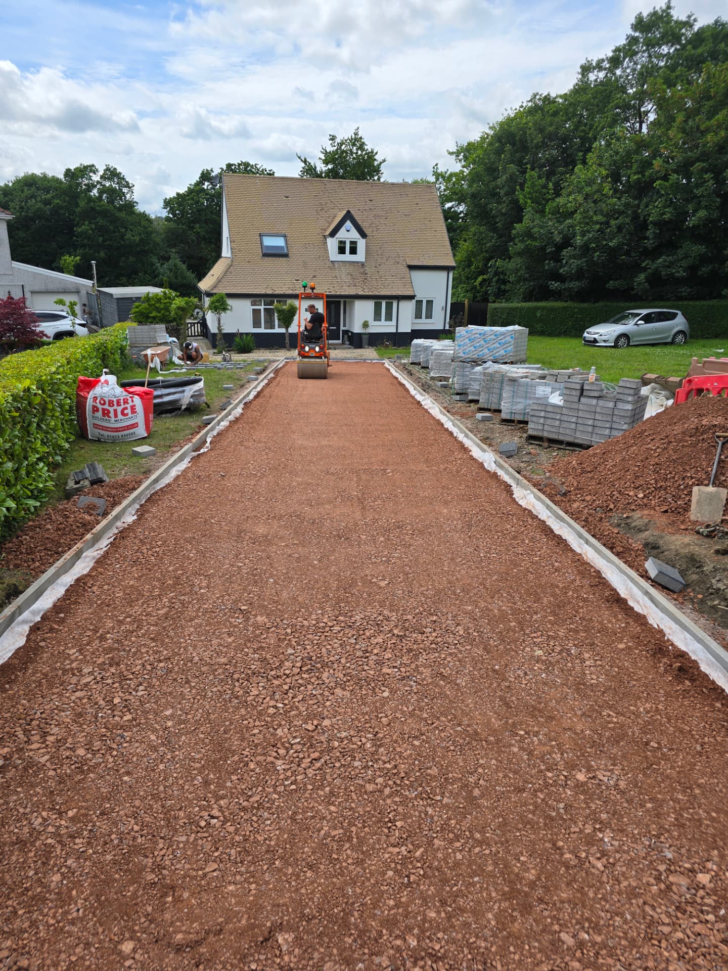 Roller compacting stone sub-base on a new driveway with materials stacked alongside