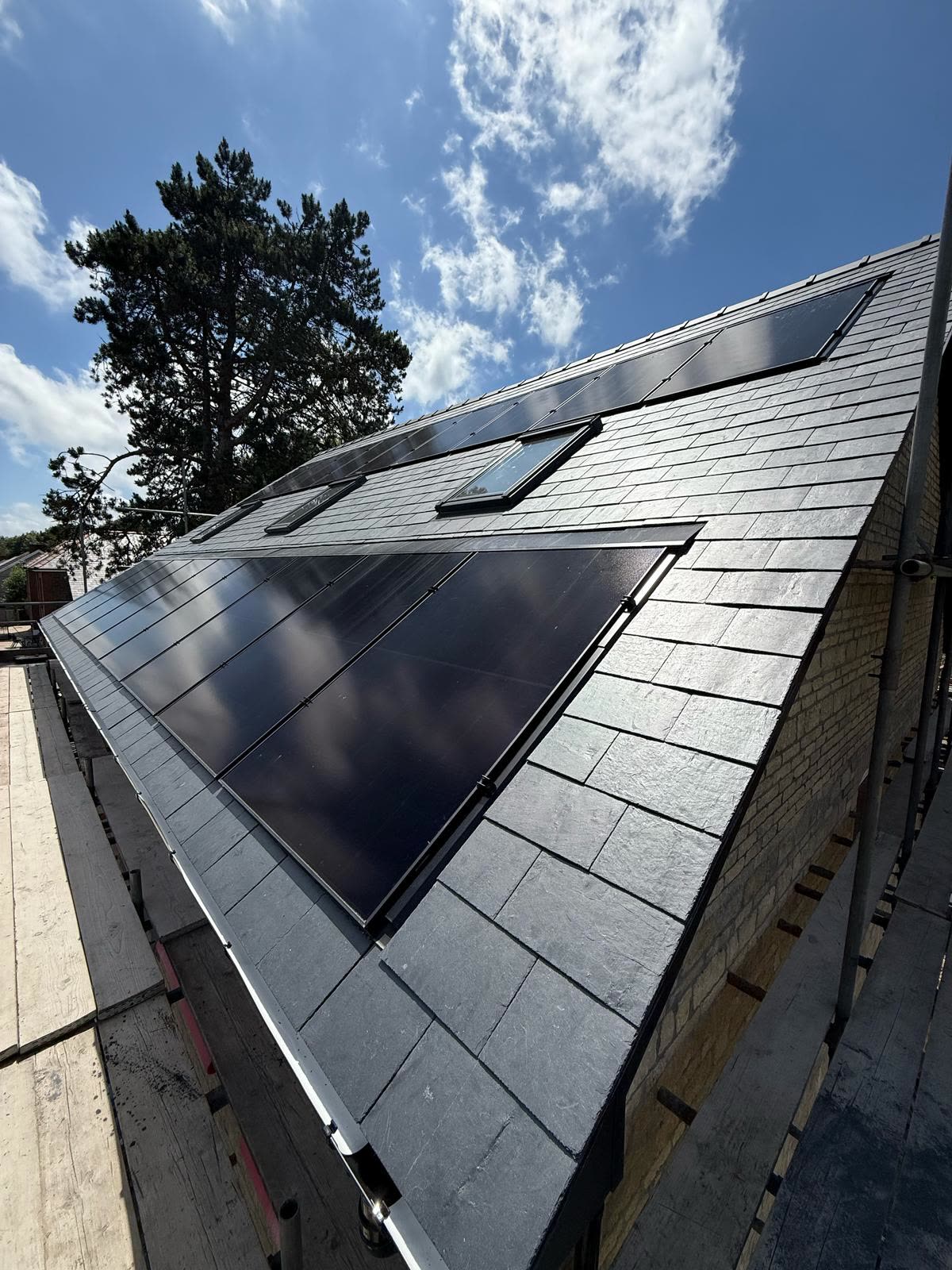 Freshly slated pitched roof with black in-roof solar panels and roof windows under blue sky