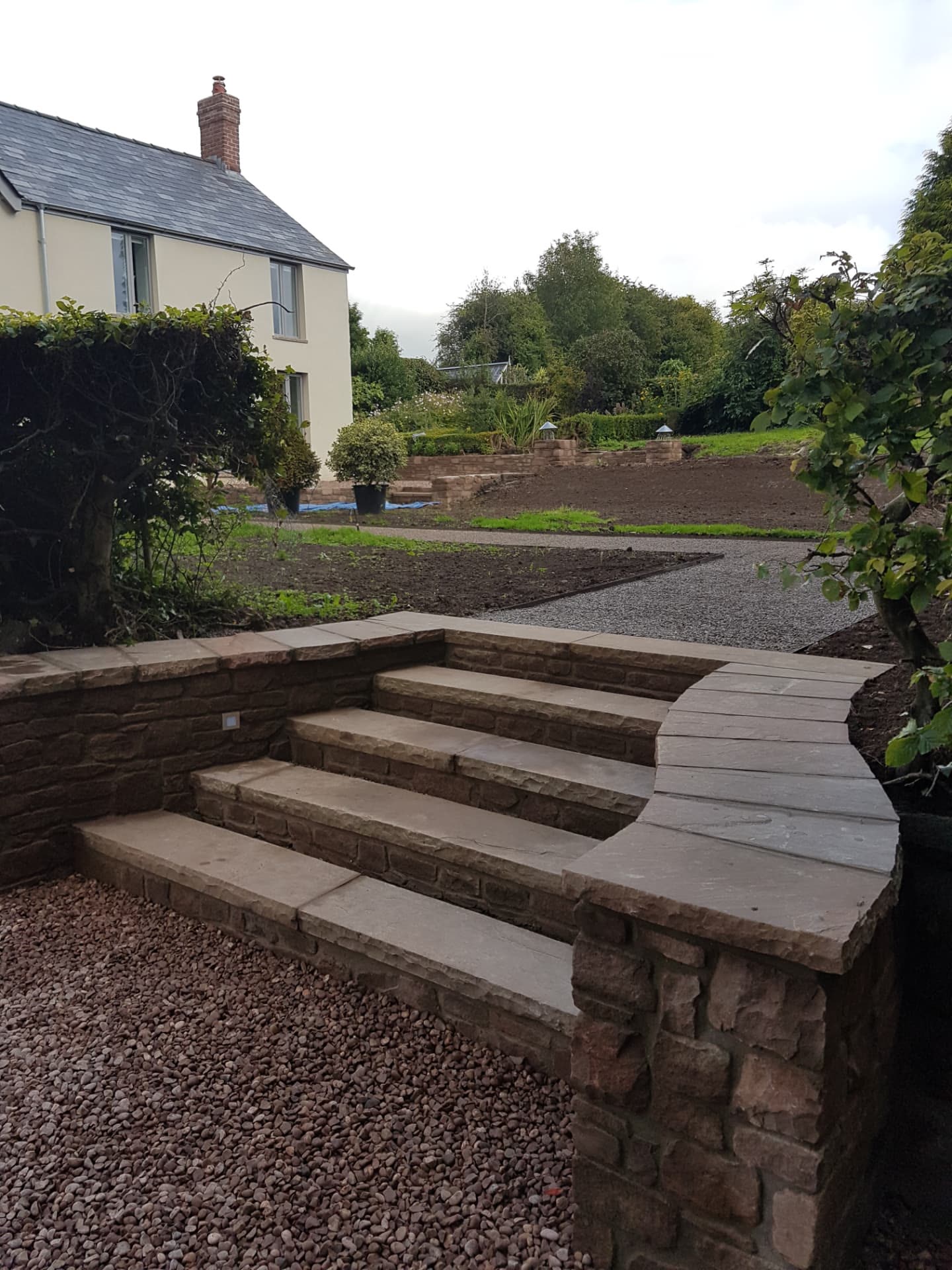 Curved sandstone steps and retaining wall leading to a landscaped garden with gravel path