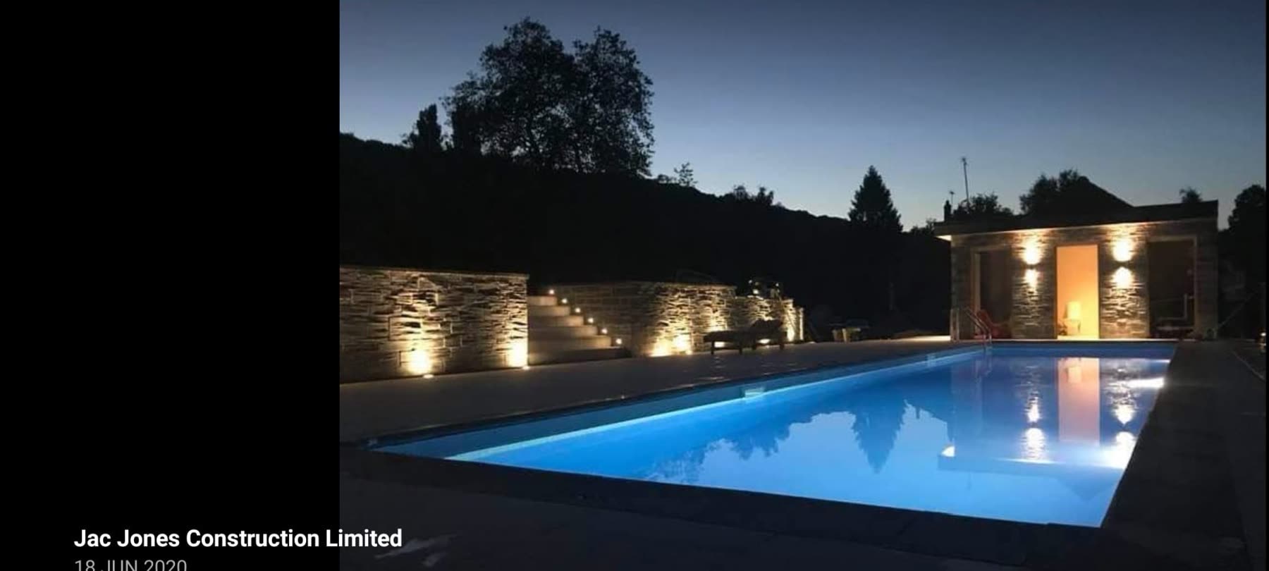 Outdoor swimming pool with underwater lighting beside stone steps and a garden building at dusk
