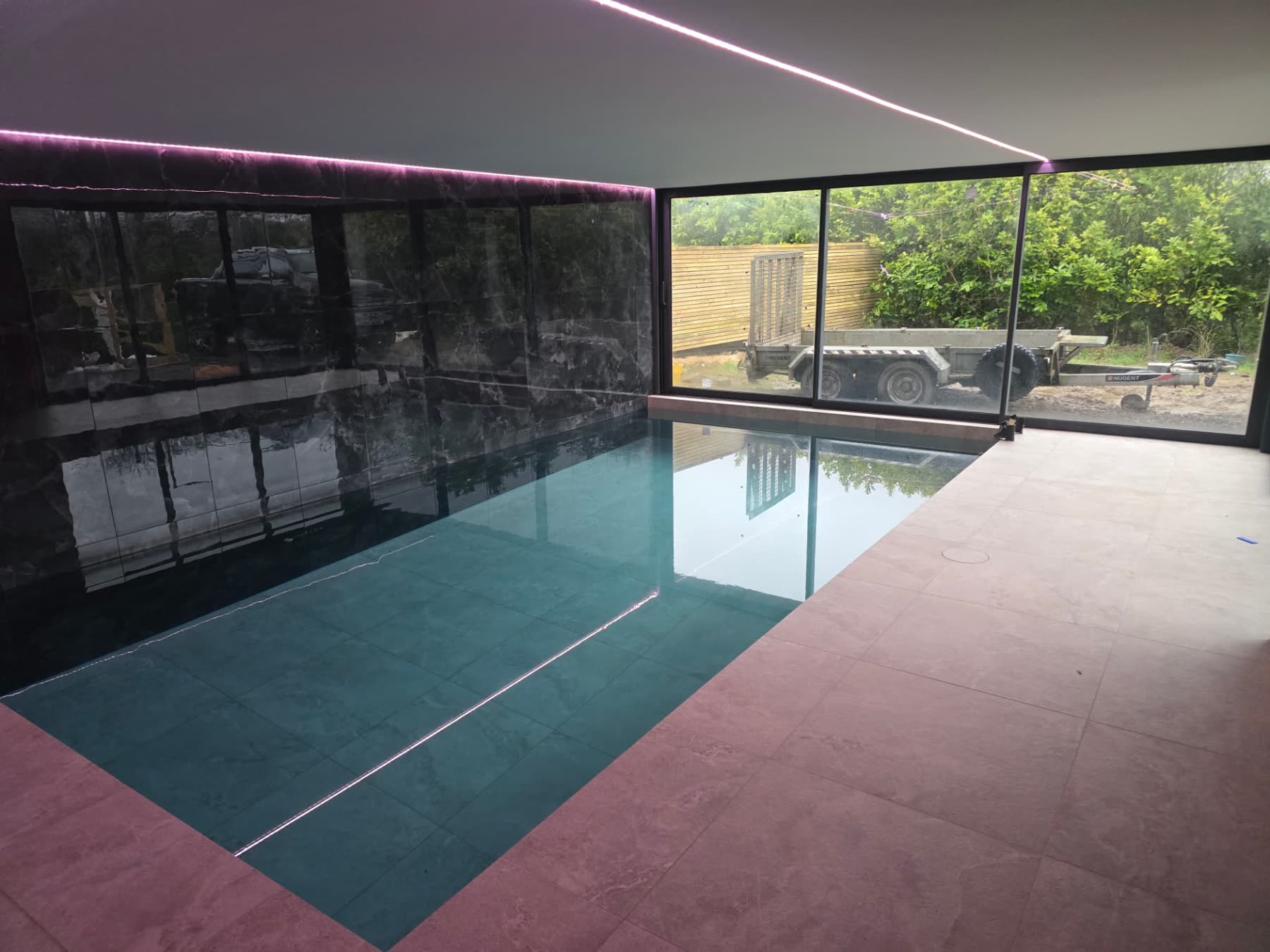 Newly built indoor swimming pool with black marble-effect wall tiles and LED lighting