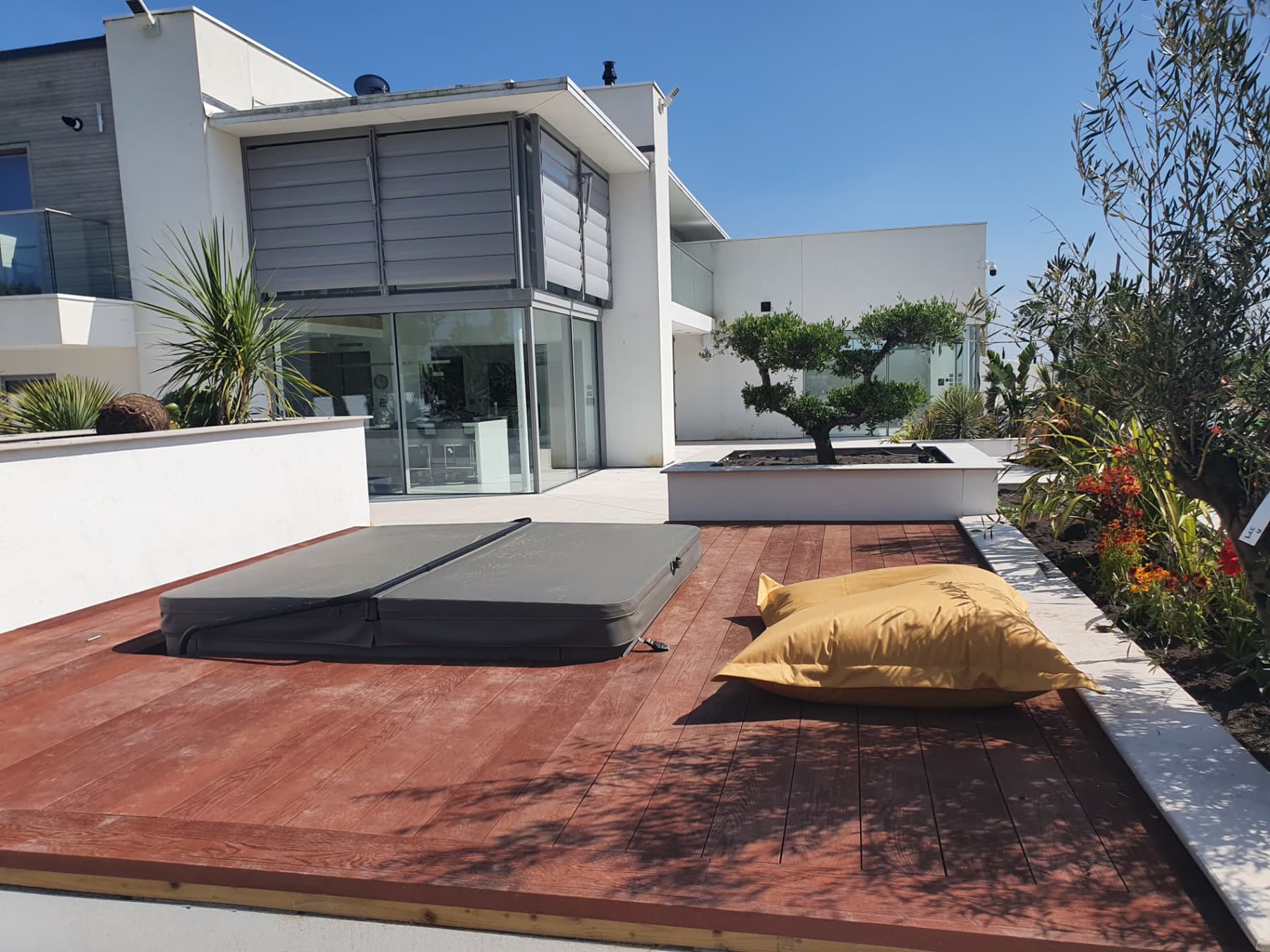 Hardwood decking with a covered hot tub and sculpted planting beside a modern house