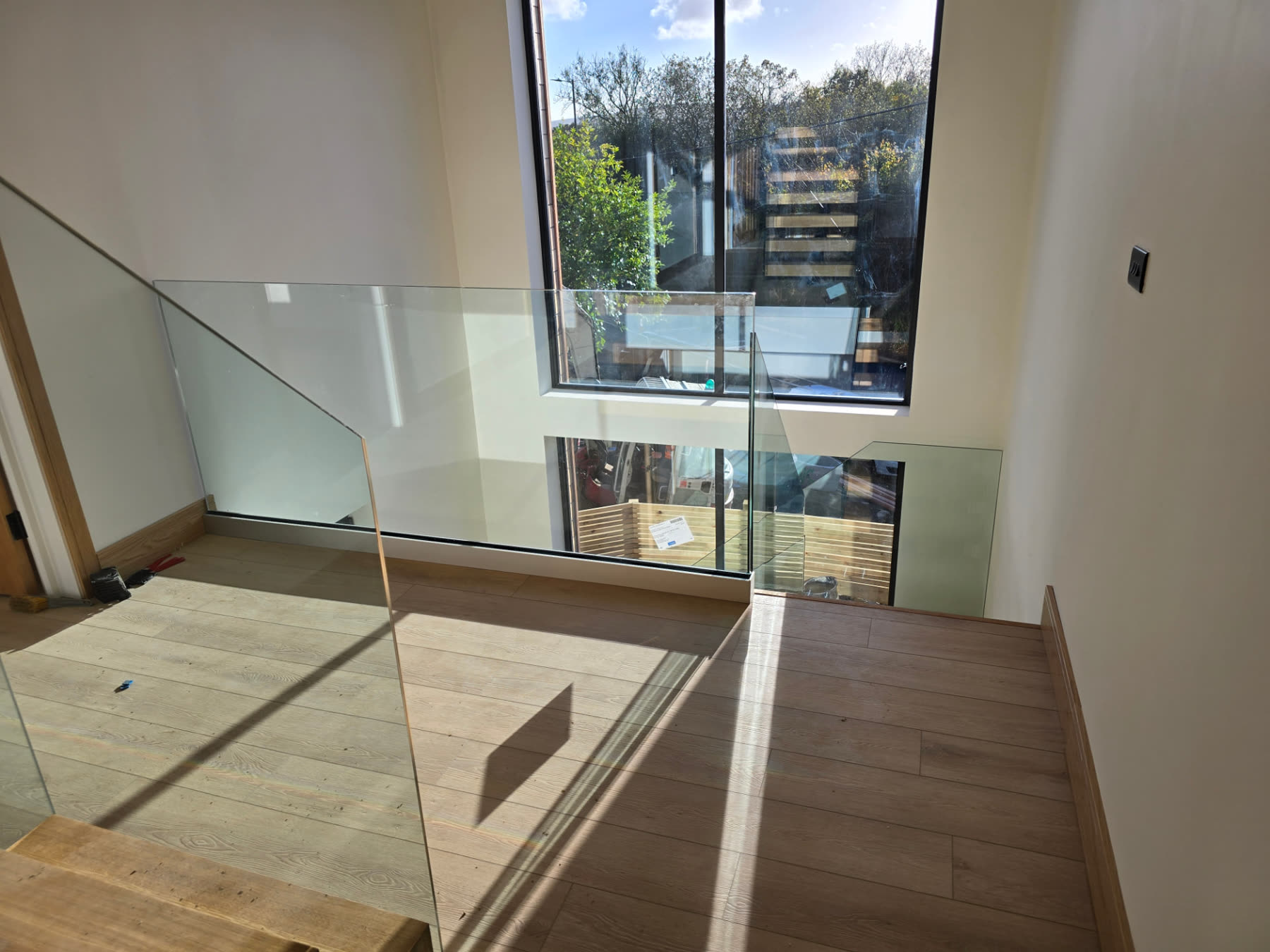 Upper landing with glass stair balustrade, wood flooring and a large window over the valley
