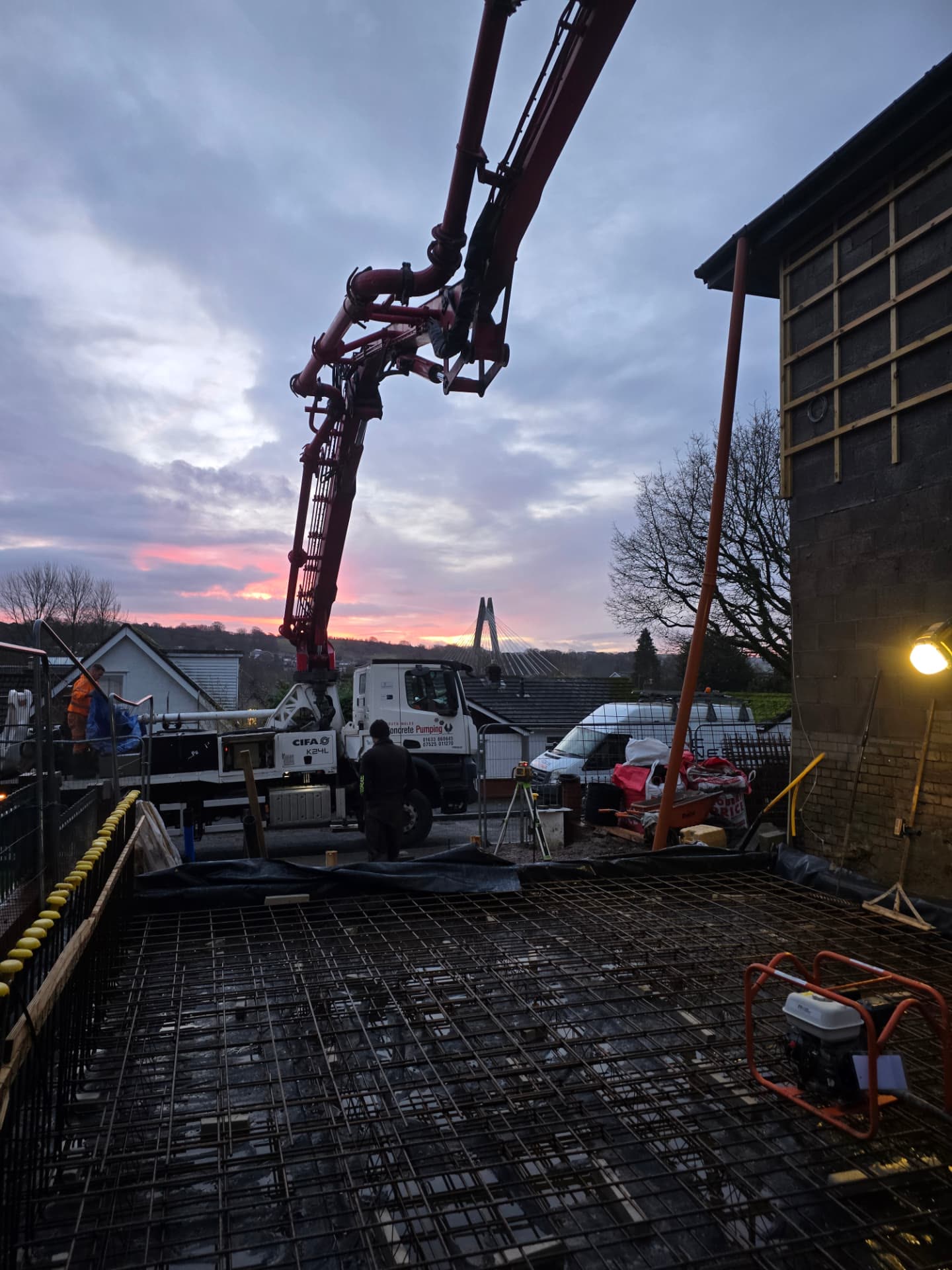 Concrete pump truck pouring a reinforced slab foundation under a bright sunrise sky
