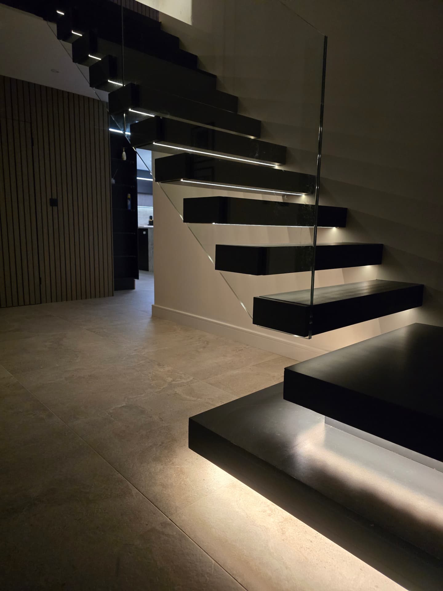 Floating staircase with LED lighting above a tiled open-plan hallway in a modern home
