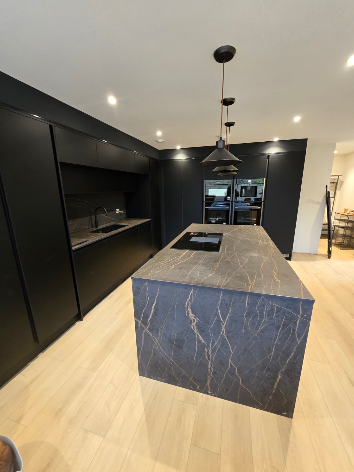 Second view of a matte black fitted kitchen with marble-effect island and pendant lighting