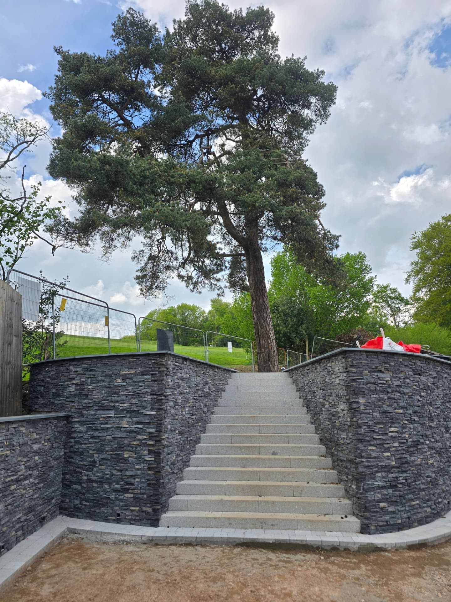 Curved natural stone retaining walls with granite steps leading up towards a large pine tree