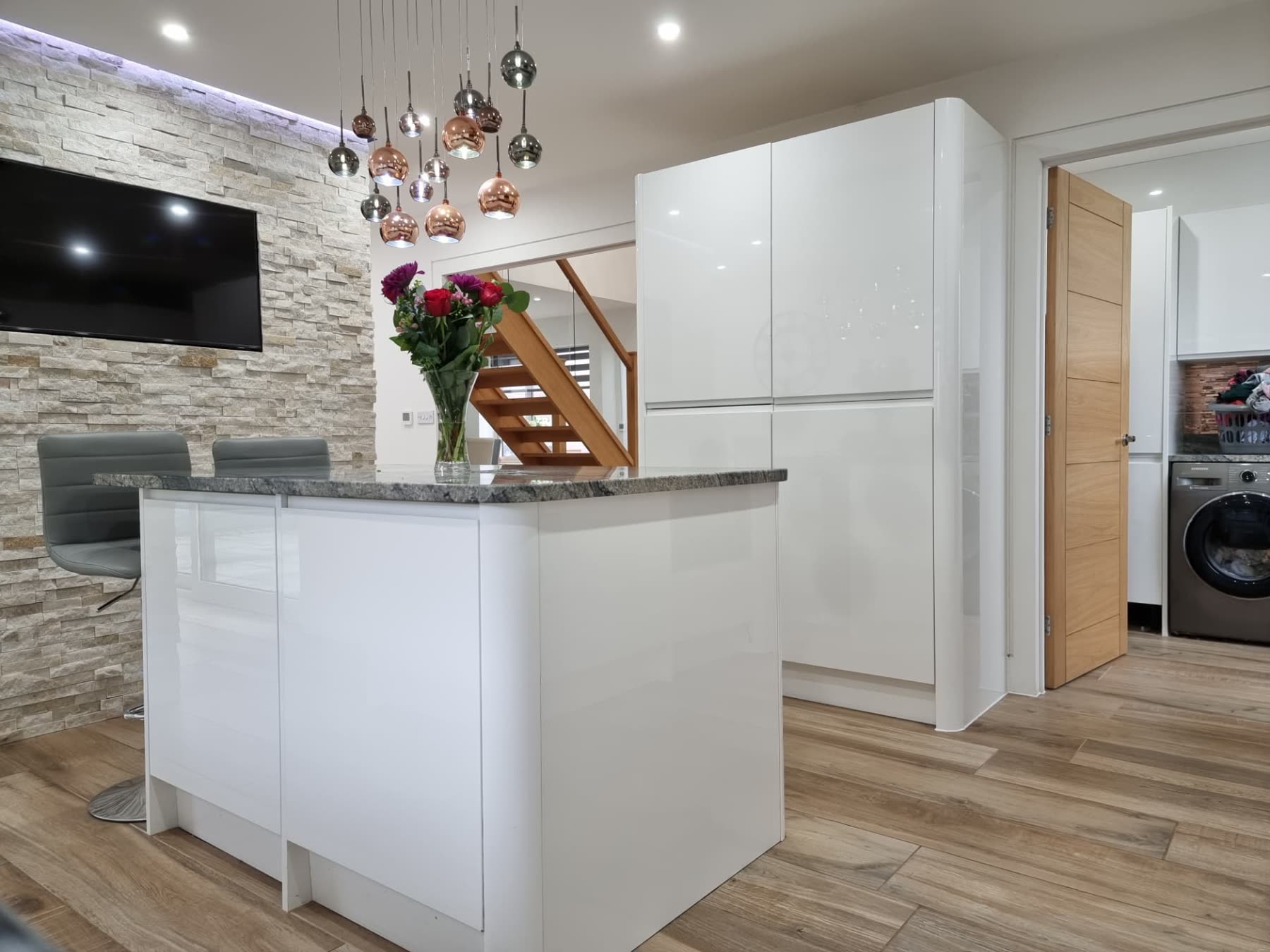 Open-plan white kitchen with copper pendant lights and a stone-clad feature wall