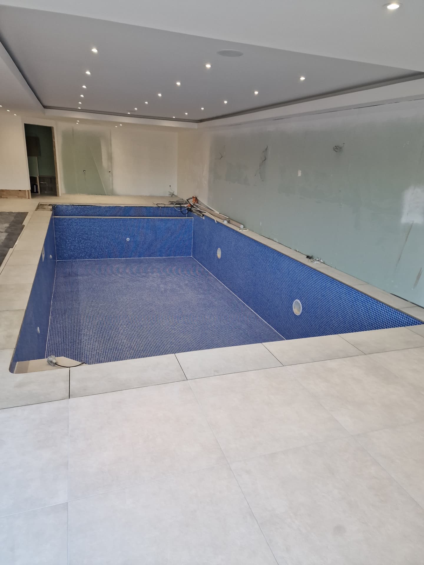 Completed indoor swimming pool with blue mosaic tiling and corner entry steps
