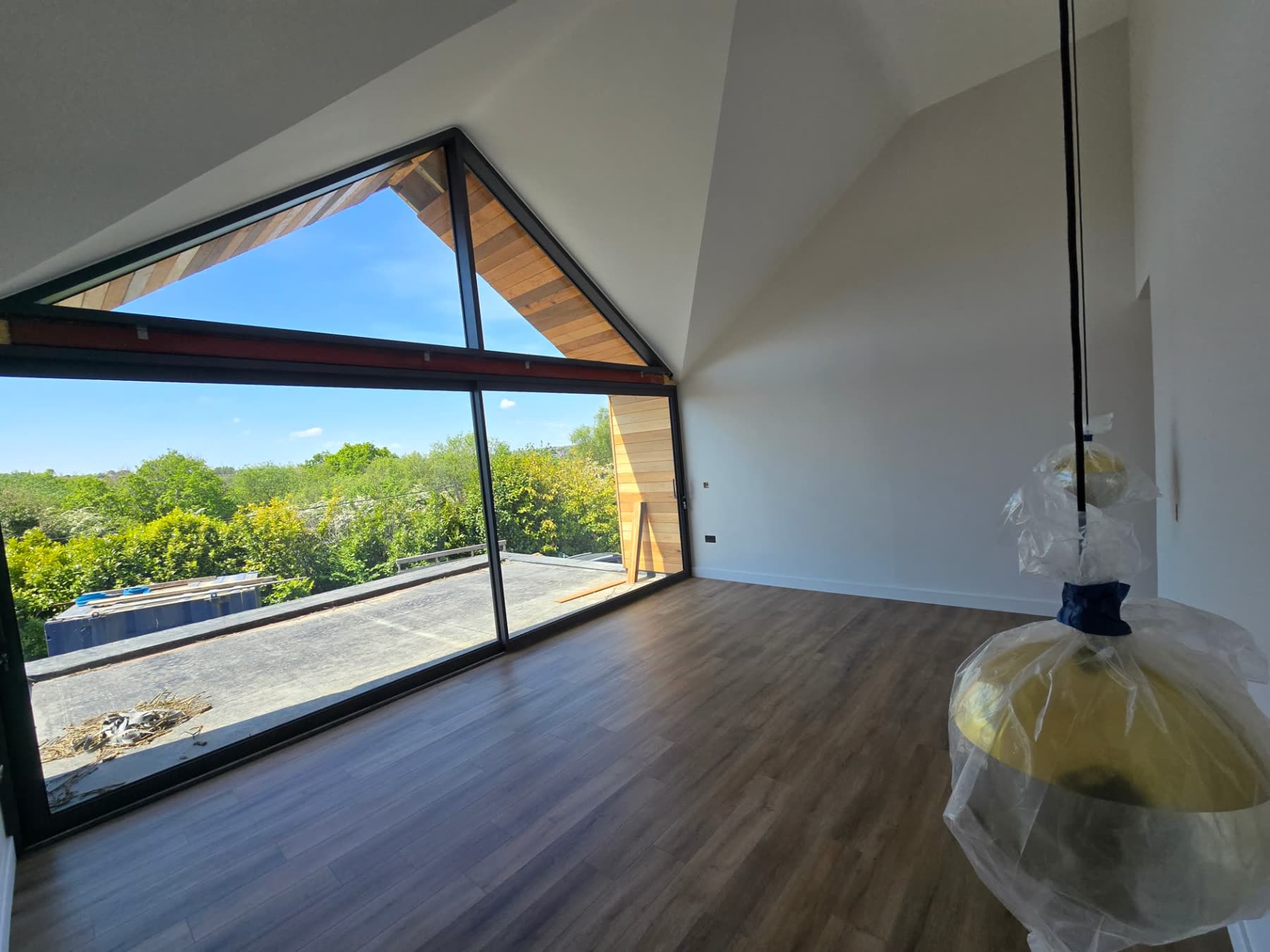 Vaulted room with black-framed apex window, timber flooring and countryside views