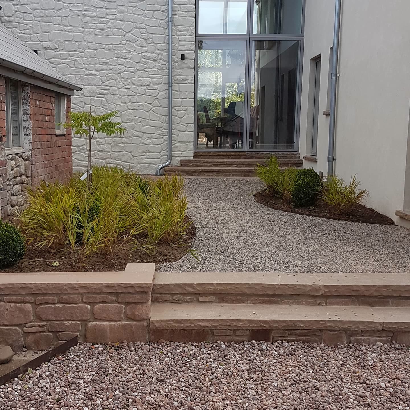 Curved gravel path with ornamental grasses leading to the glazed doors of a stone-clad house