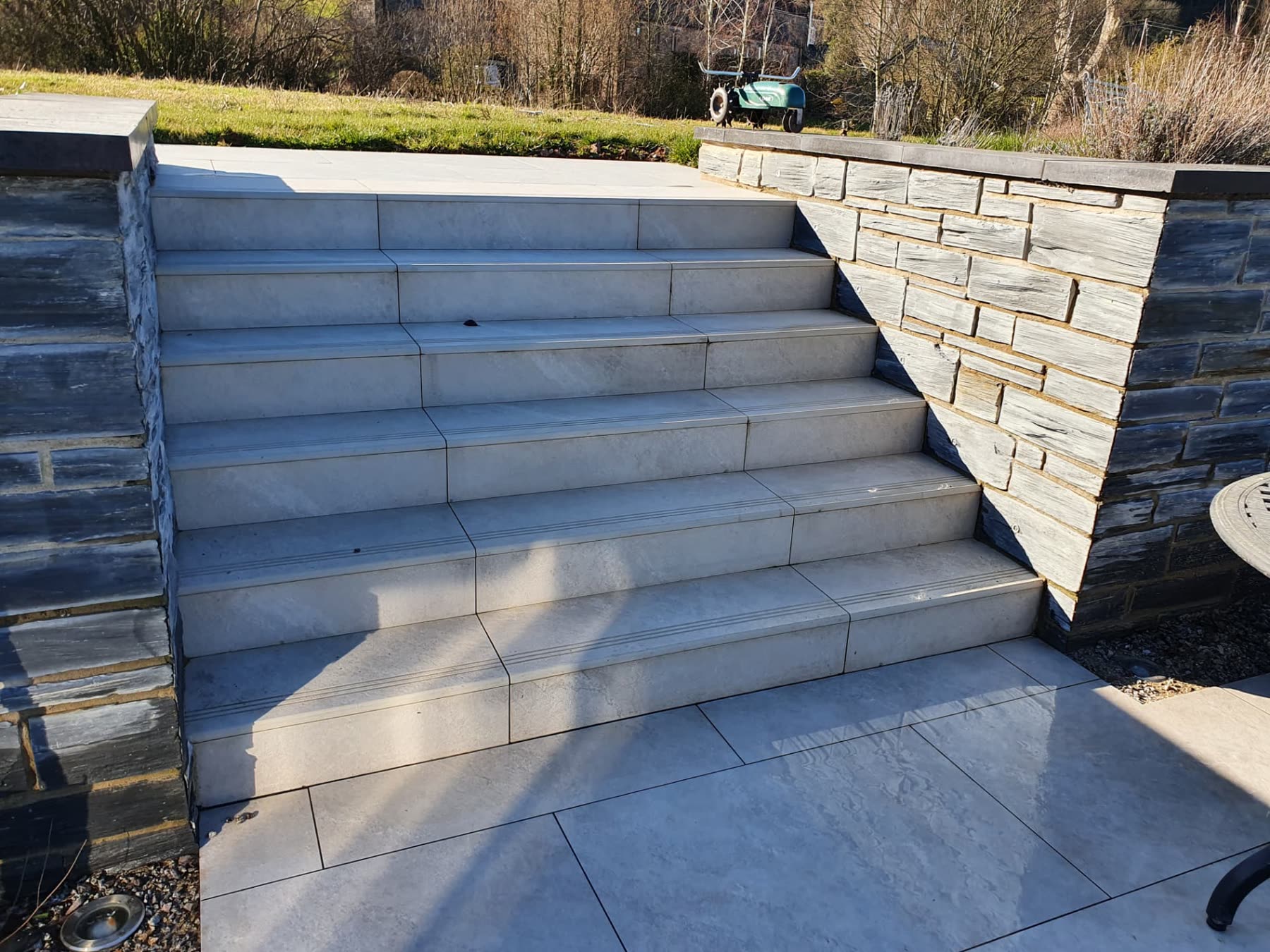 Broad stone steps flanked by stacked stone walls connecting two paved terrace levels