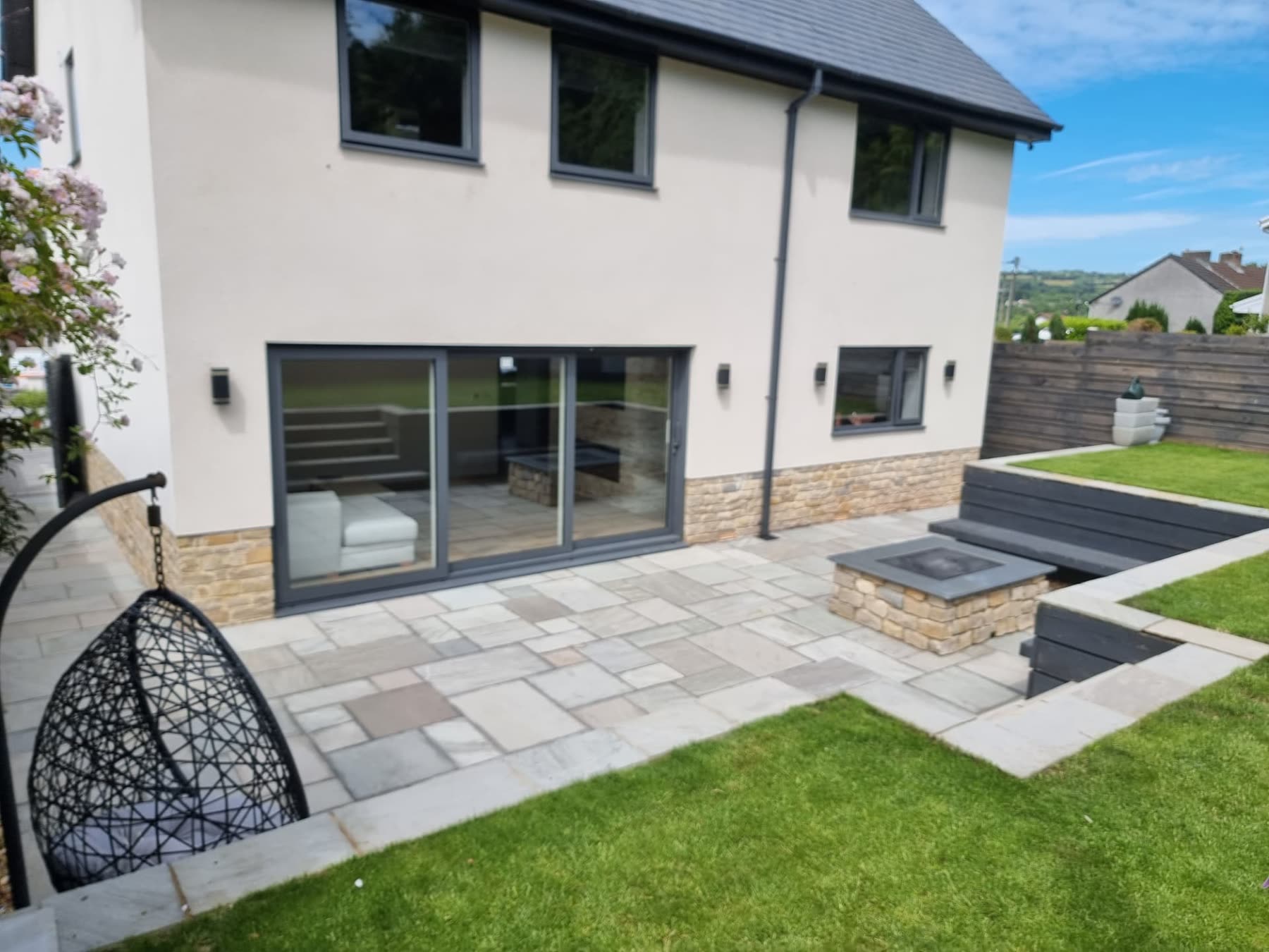 Rear garden patio with a stone-clad fire pit, built-in bench seating and lawn