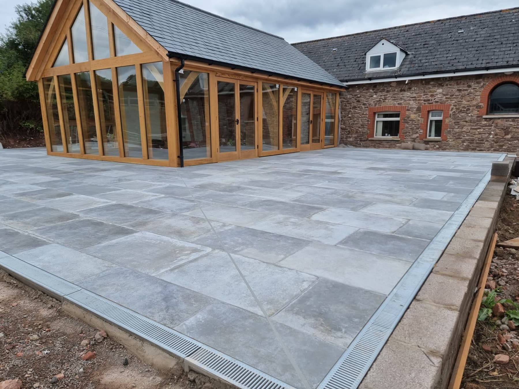Completed oak-framed glazed garden room extension with new stone paving and drainage channels