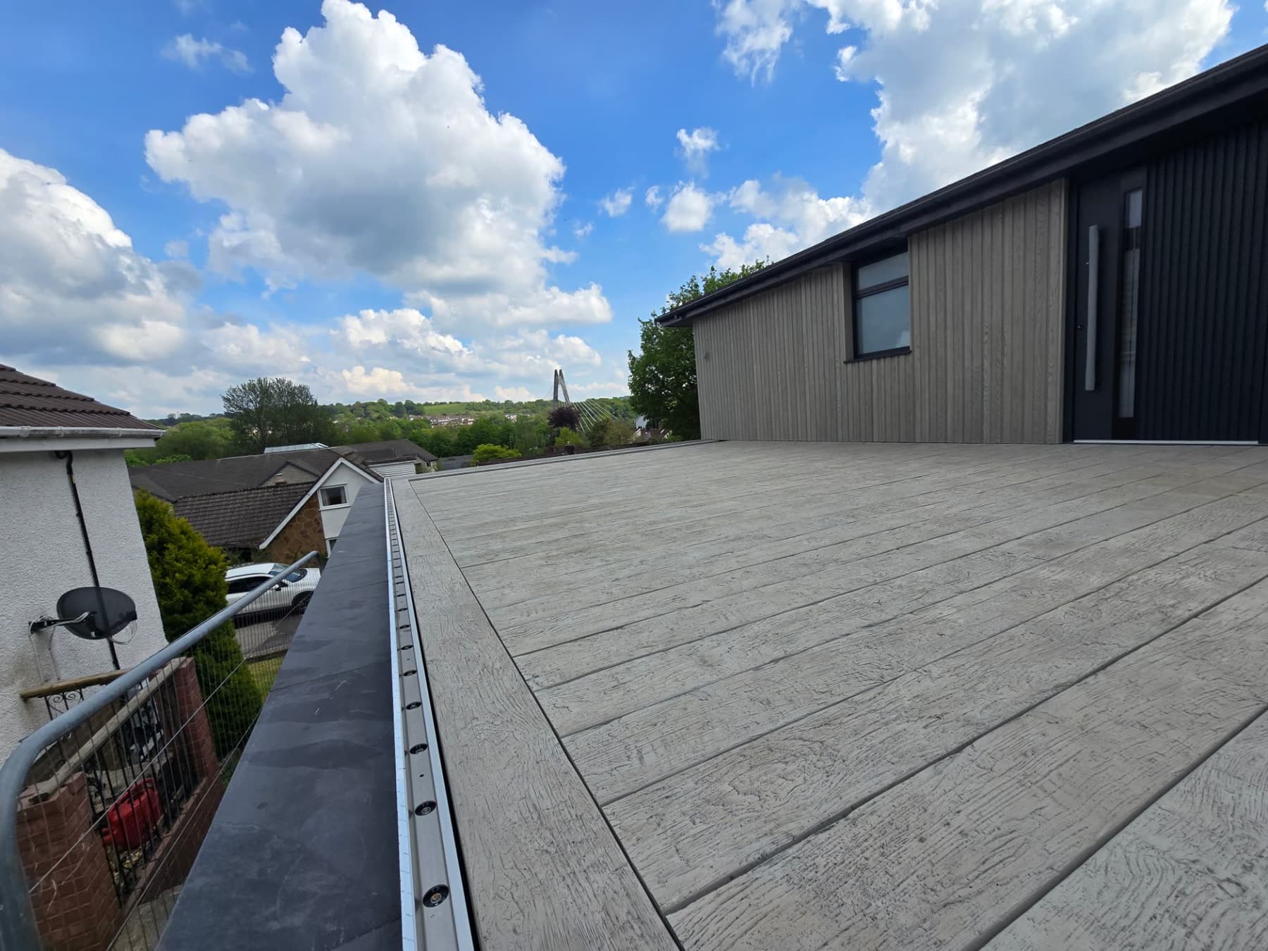 Newly installed flat roof with wood-effect membrane finish on a modern timber-clad extension