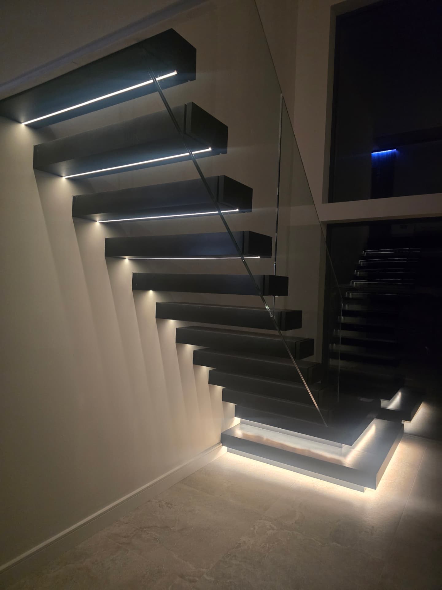 Modern floating timber staircase with glass balustrade and integrated LED strip lighting