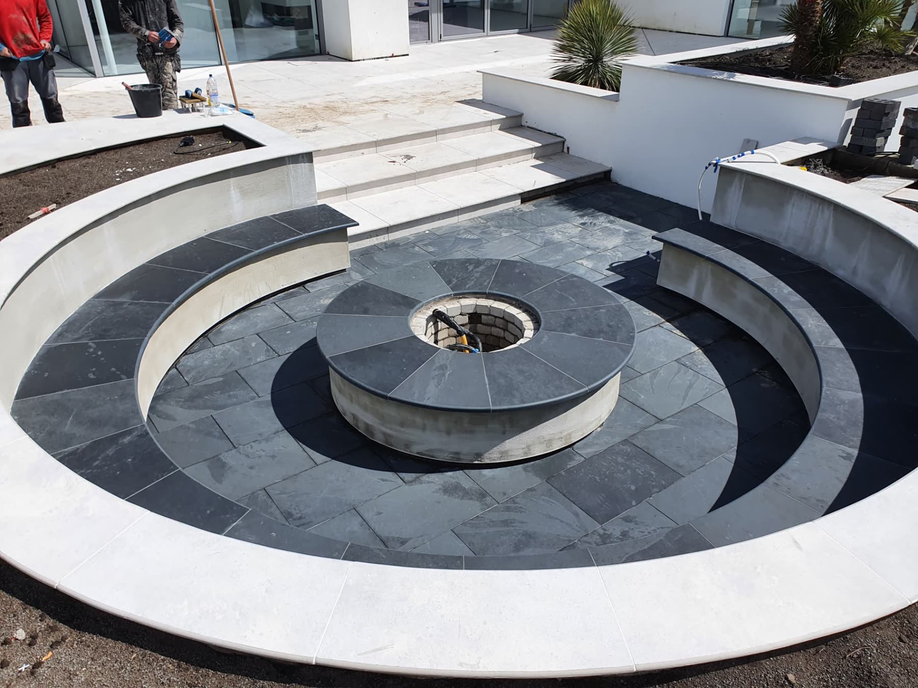 Round fire pit terrace with dark stone paving and curved rendered seating walls