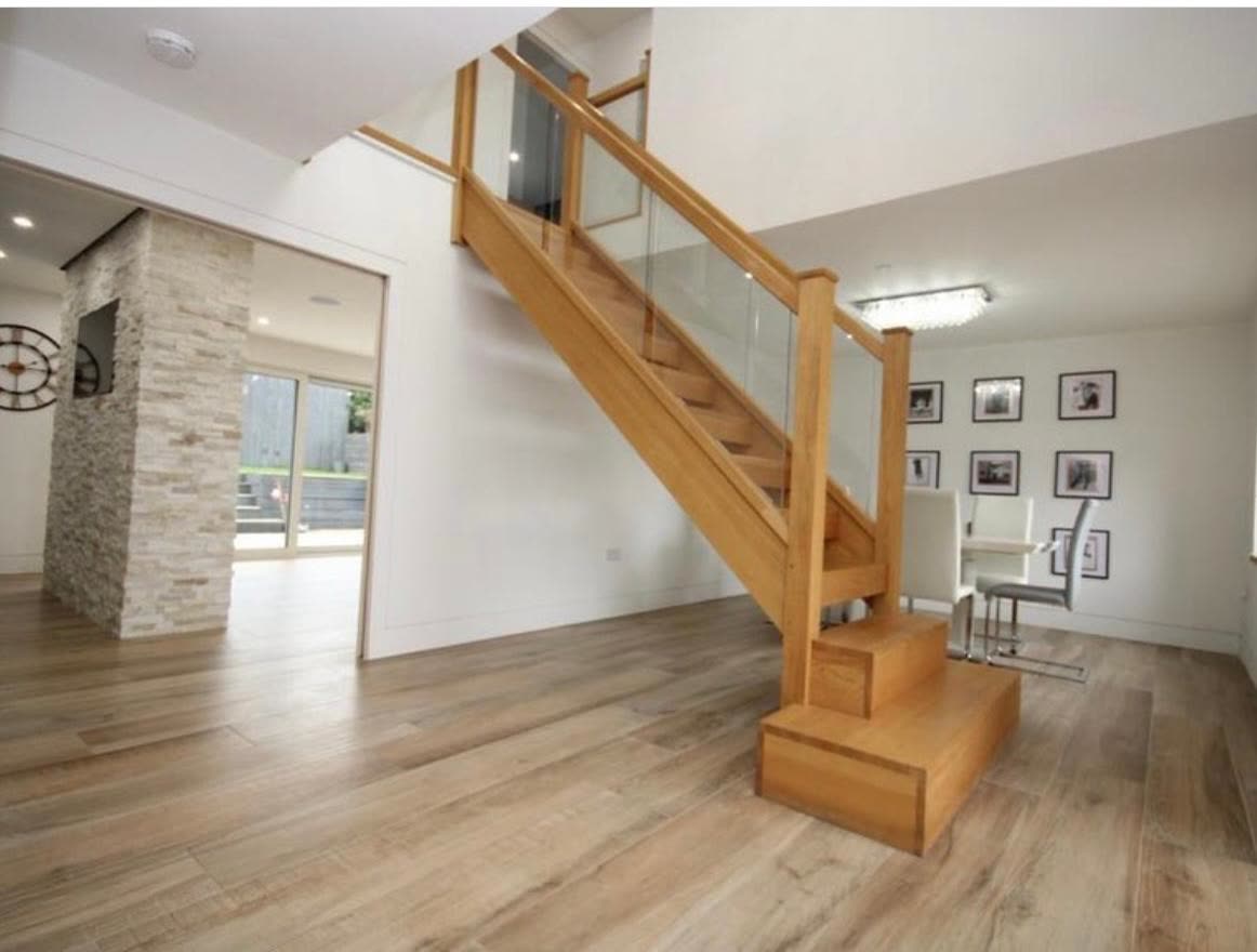 Oak staircase with glass balustrade panels in a bright hallway with wood-effect flooring