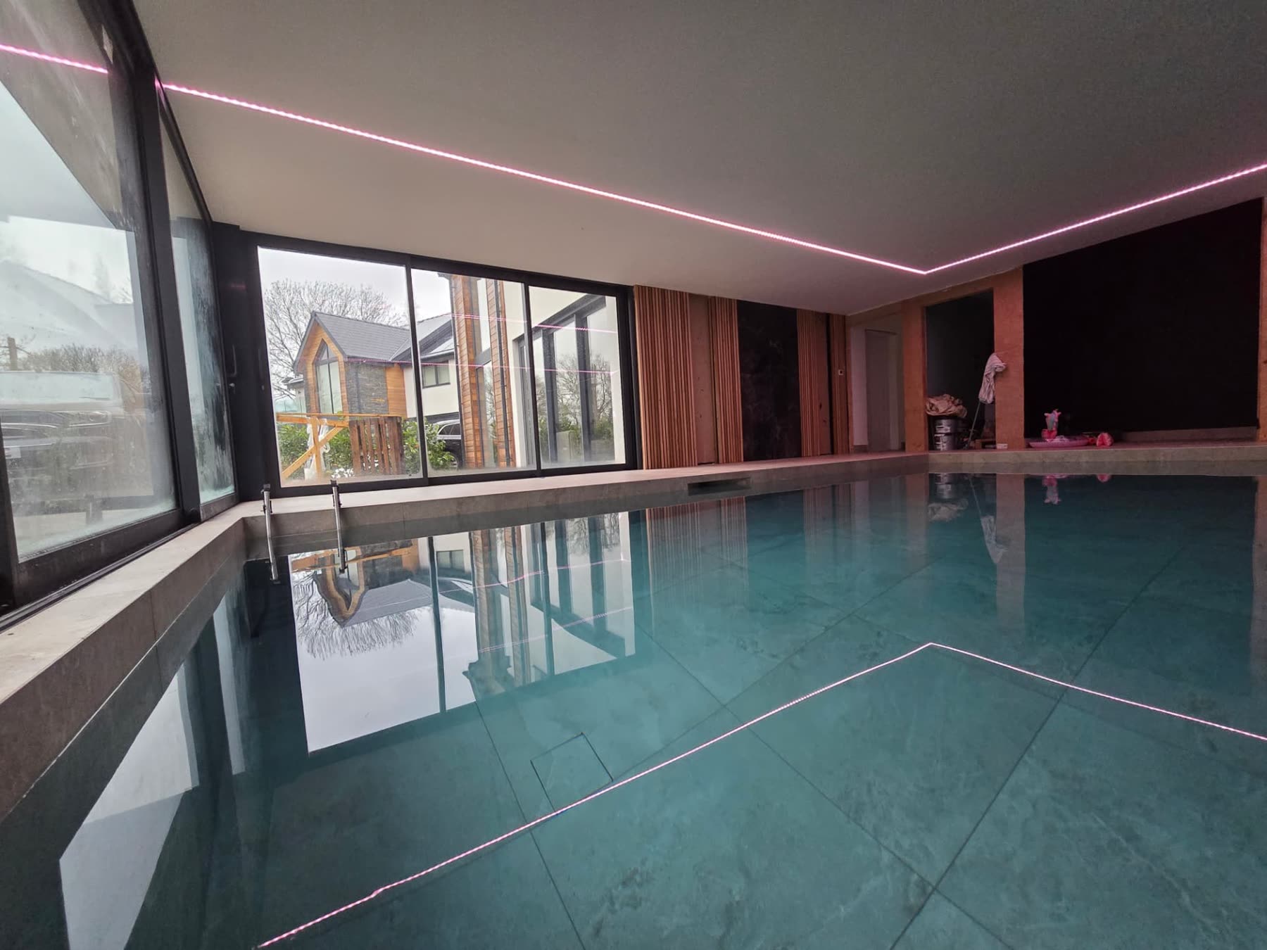 Large indoor swimming pool with LED lighting and a glazed wall overlooking the countryside
