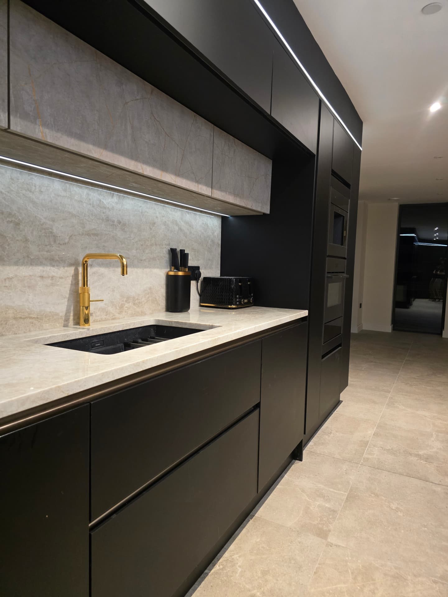 Modern black fitted kitchen with brass tap, marble splashback and built-in ovens