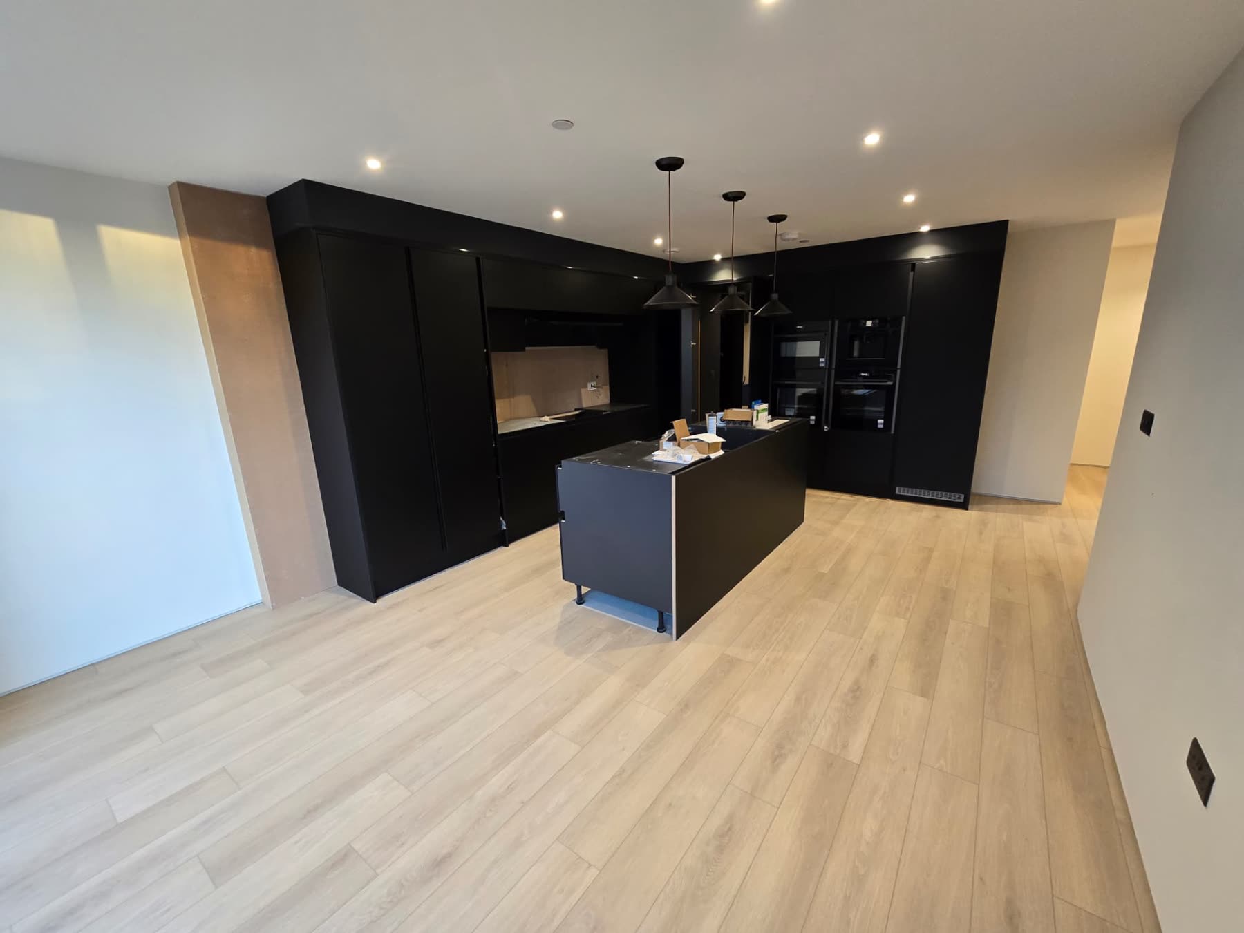 Matte black fitted kitchen with island, integrated ovens and light oak flooring in a new home