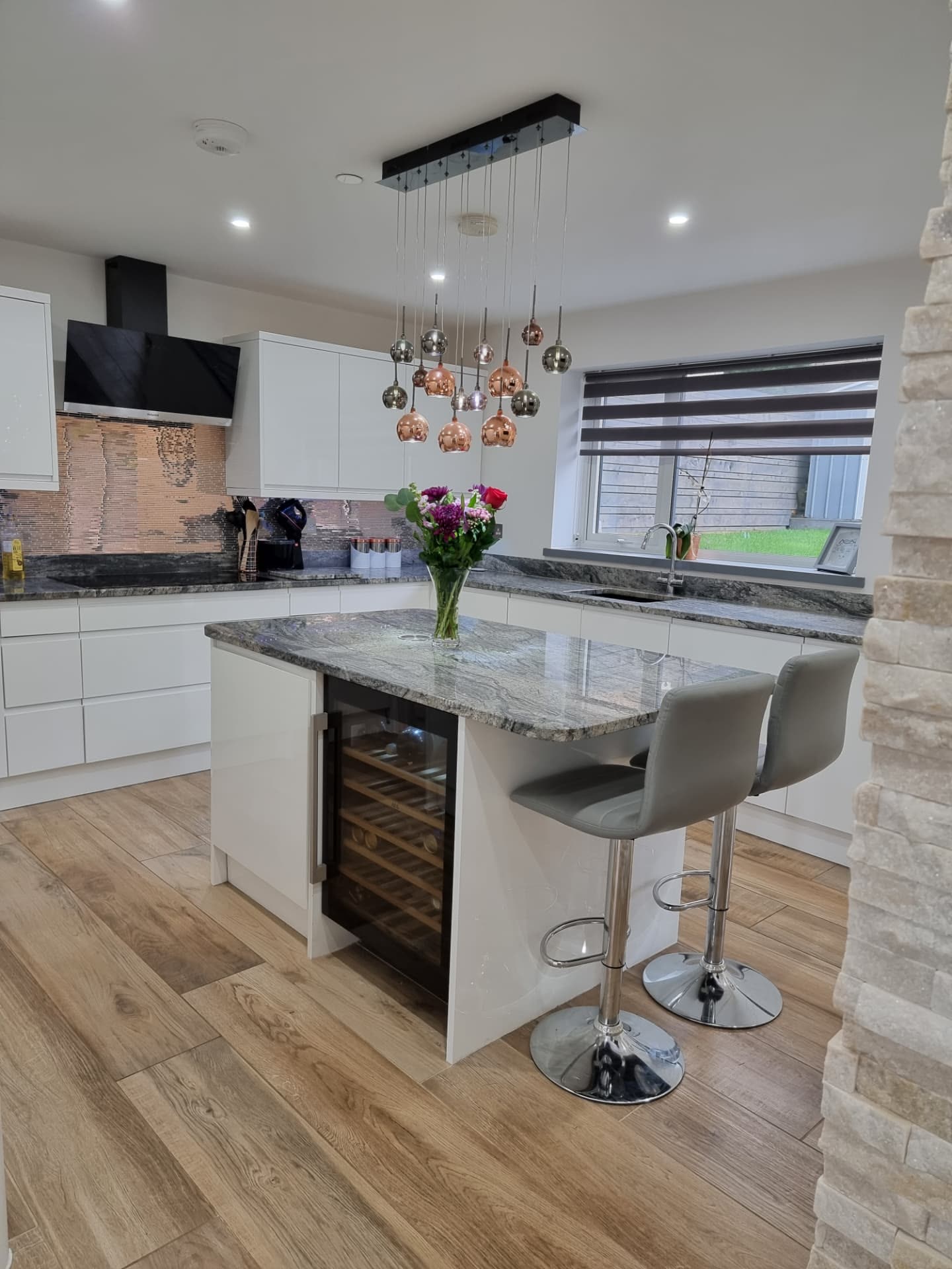 Modern white gloss kitchen with stone island, copper pendant lights and oak flooring