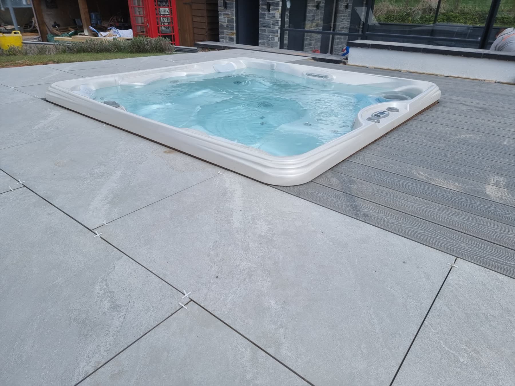 Newly installed hot tub sunk into porcelain paving beside a glazed pool enclosure