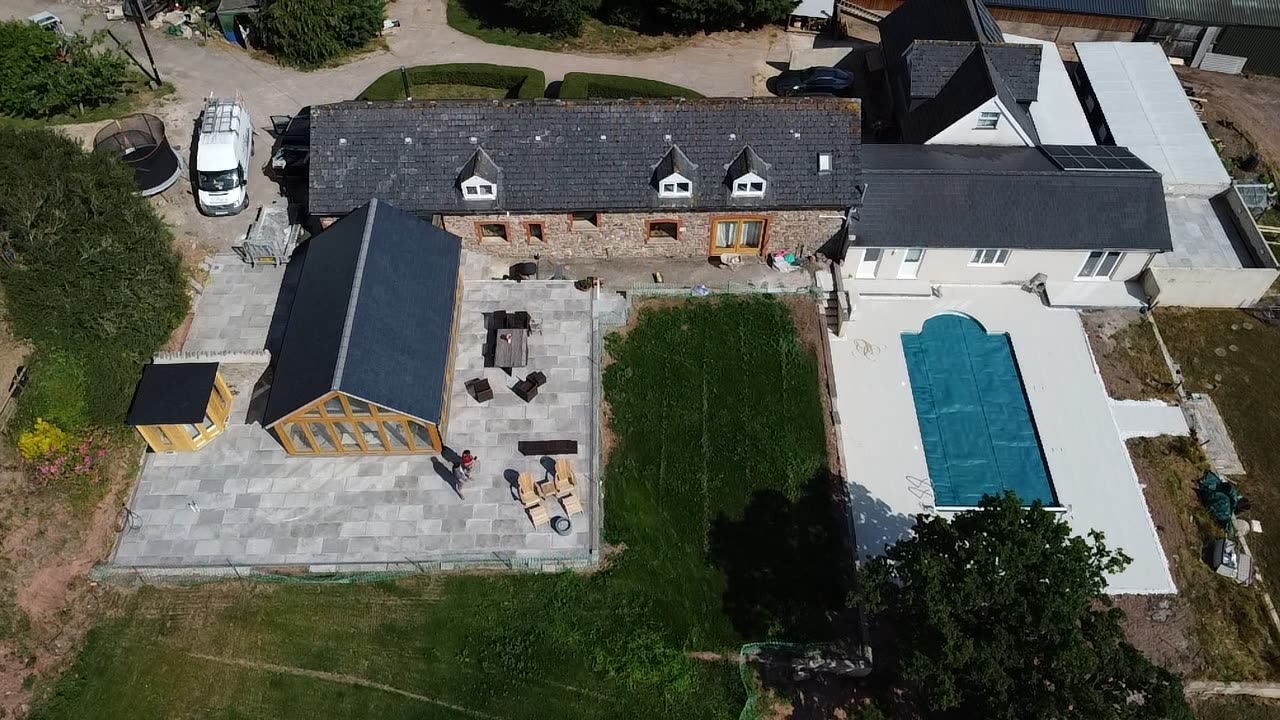 Aerial view of a stone barn conversion with paved courtyard, garden room and covered swimming pool