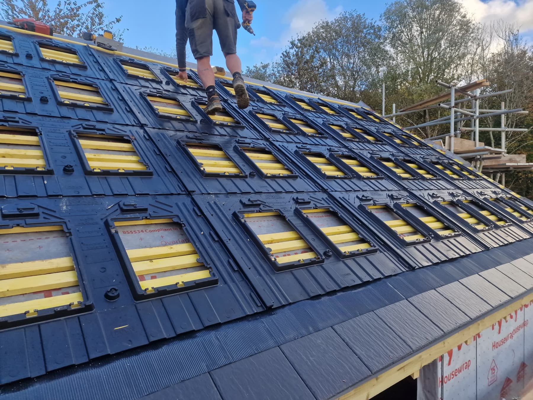 Roofer installing integrated solar panels into a slate-effect tiled roof