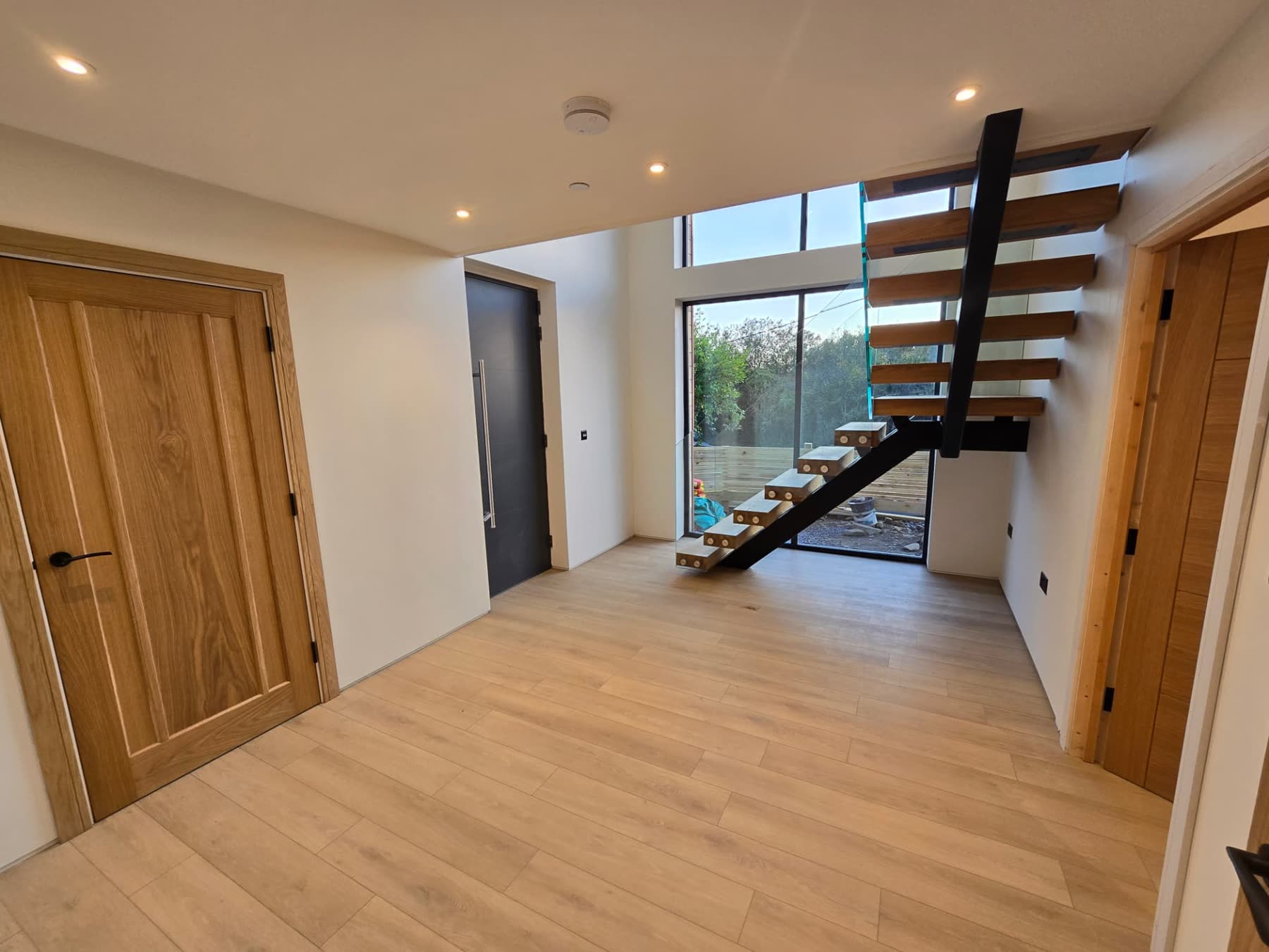 Open-plan hallway in a bespoke home with cantilevered timber staircase and glazed entrance