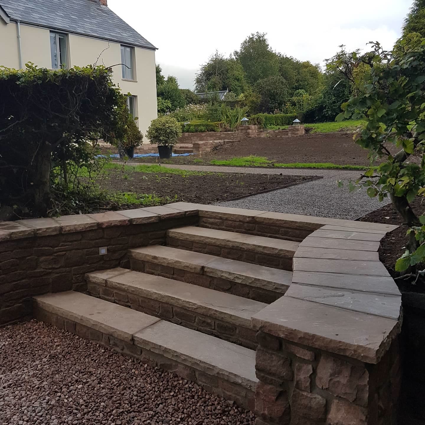 Curved sandstone steps and retaining wall linking a patio to a gravel driveway and lawn